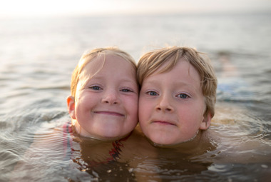 A girl and boy submerged in a lake up to their chins, smiling